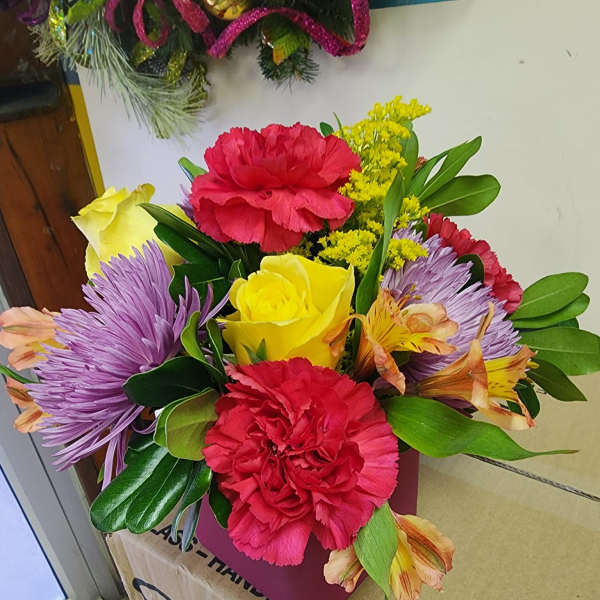 Mixed bouquet with red carnations, yellow roses, and purple flowers in a pink box
