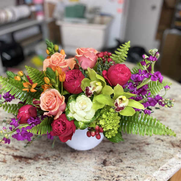 Mixed bouquet of roses, orchids, and purple flowers in a white vase