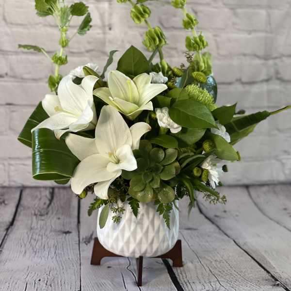 White lilies and green succulents arranged in a white vase