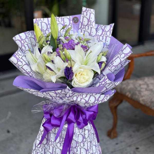 Purple and white bouquet with lilies and roses wrapped in patterned paper
