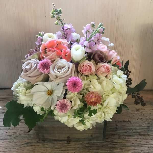 Mixed bouquet in a wooden box with roses, hydrangeas, and pastel blooms