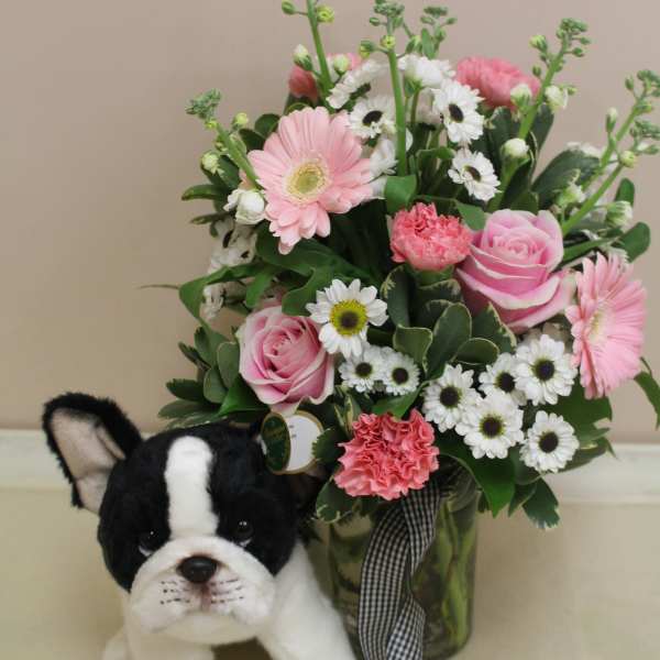Pink and white flower arrangement with a plush dog in front