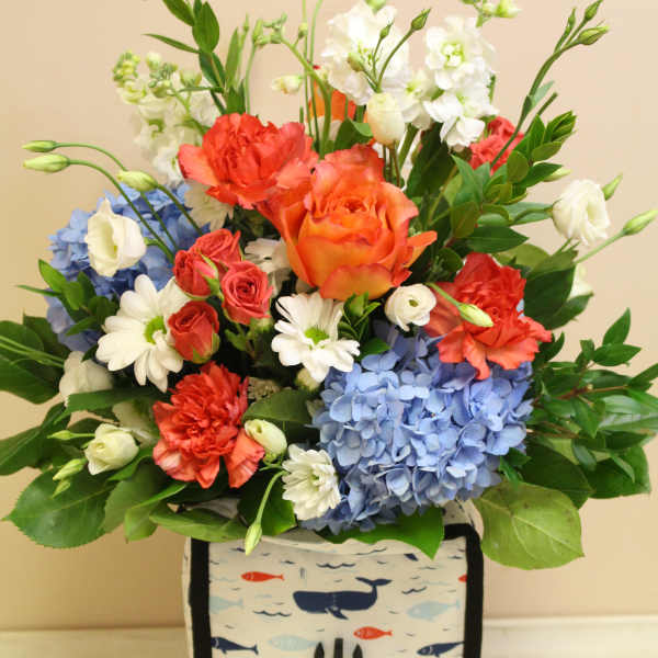 Mixed bouquet of roses, carnations, hydrangeas, and daisies in a patterned lunch bag