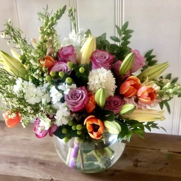 Mixed bouquet of roses, lilies, and tulips in a glass bowl vase