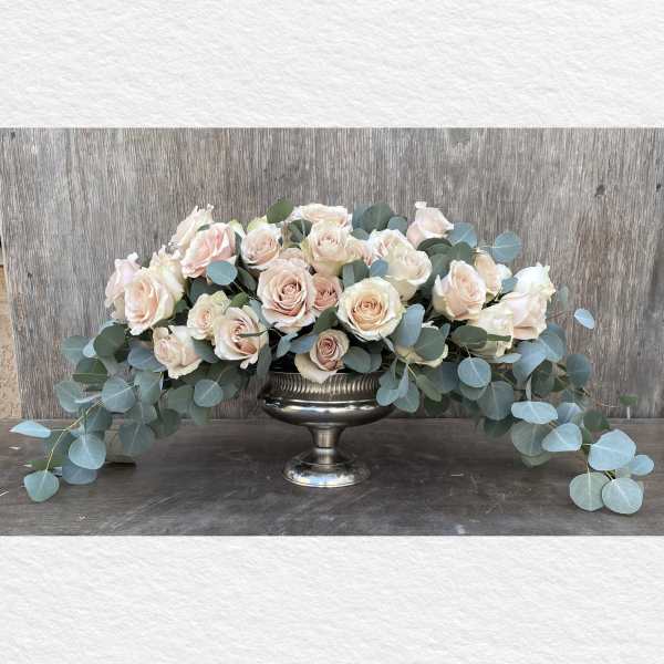 Blush roses arranged in a silver pedestal bowl with trailing eucalyptus