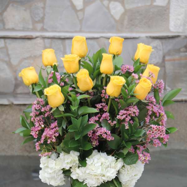 Yellow roses and pink flowers in a tall glass vase