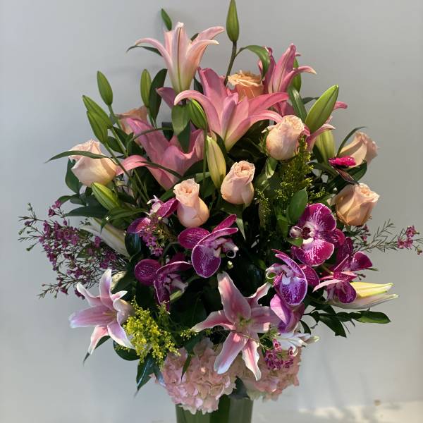Pink lilies, roses, and orchids arranged in a tall glass vase