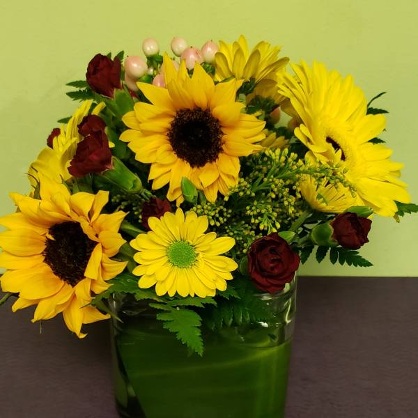 Sunflower and burgundy rose arrangement in a green glass vase