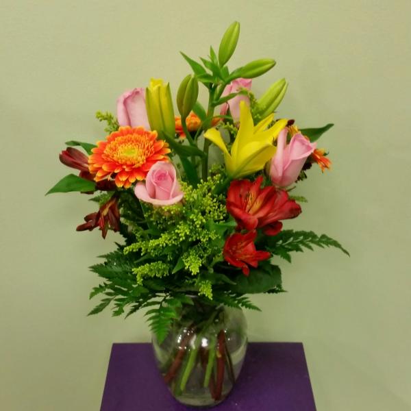 Mixed bouquet of lilies, roses, and gerbera daisies in a glass vase