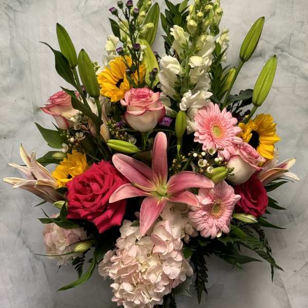 Mixed bouquet with pink roses, lilies, gerberas, sunflowers, and hydrangea in a glass vase