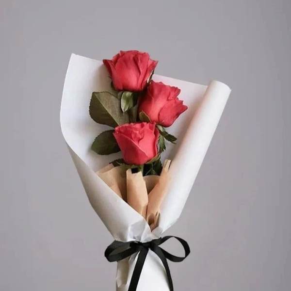 Three red roses wrapped in white paper with a black ribbon