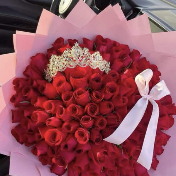 Large bouquet of tightly packed red roses with jeweled tiara, wrapped in pink paper with white ribbon