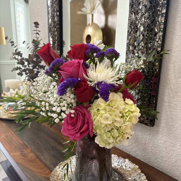 Mixed bouquet of roses, hydrangea, and white daisy-like blooms in a dark vase