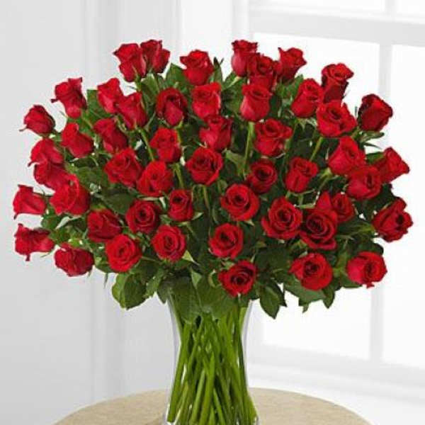 Large bouquet of long-stem red roses arranged in a clear glass vase on a table