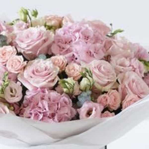 Bouquet of pale pink roses and ruffled pink flowers wrapped in white paper