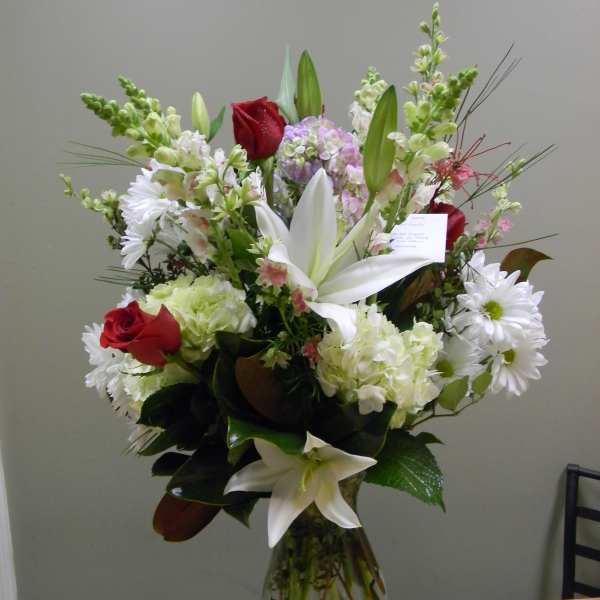 Tall mixed bouquet with red roses, white lilies, and white daisies in a glass vase