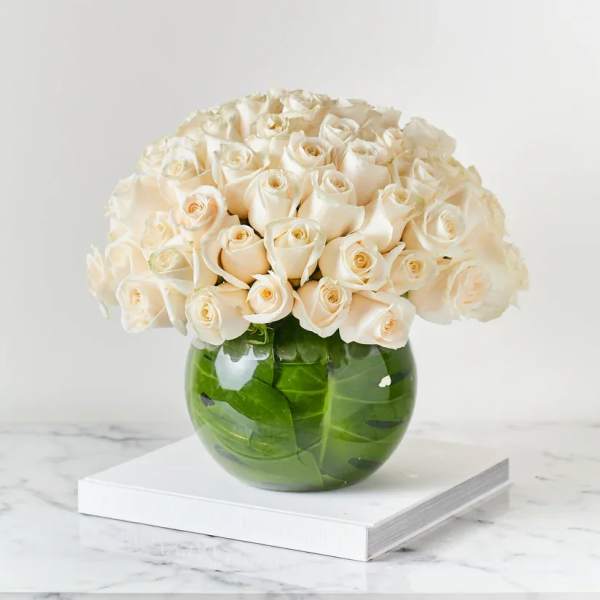 Cream roses arranged in a round green glass vase