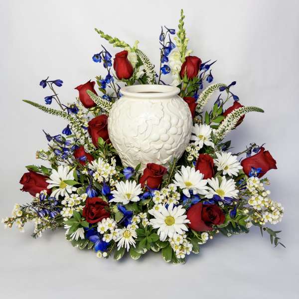 Red roses and white daisies arranged around a white urn vase