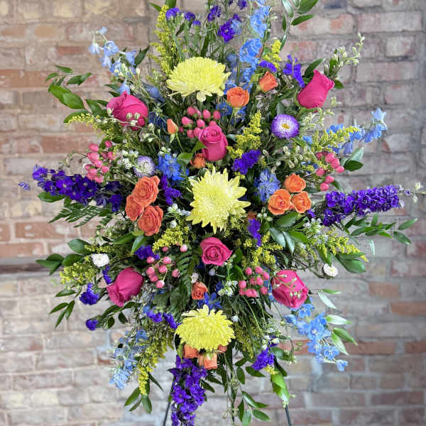 Tall mixed flower arrangement with pink roses, yellow mums, and blue-purple blooms