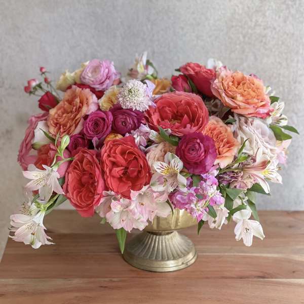 Mixed pink and coral flowers arranged in a gold pedestal vase