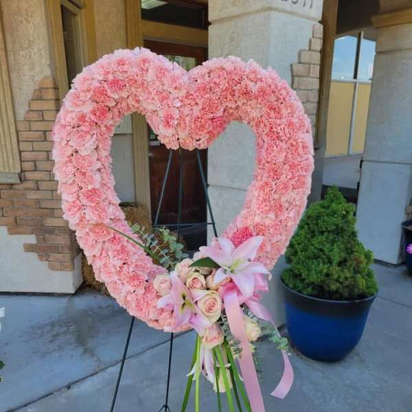 Pink heart-shaped floral wreath on a stand with a small rose bouquet