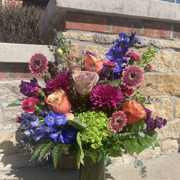 Colorful mixed bouquet in a glass vase with roses and blue flowers