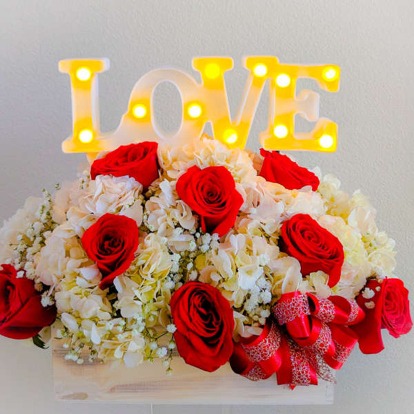 Red roses and white hydrangeas arranged with a lit LOVE sign