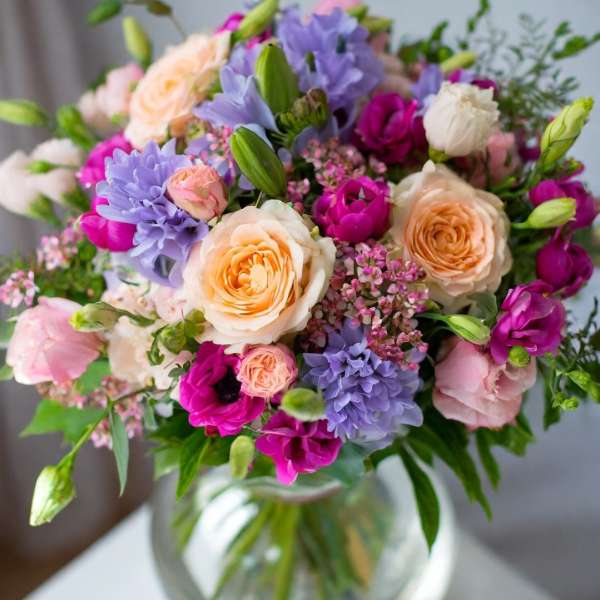 Mixed bouquet of peach, pink, and purple flowers in a glass vase