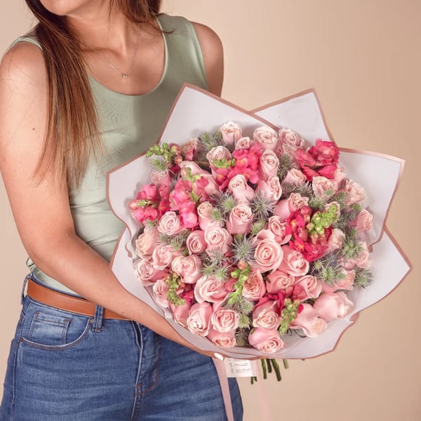Woman holding a large bouquet of pink roses and snapdragons wrapped in white paper