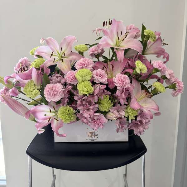 Pink lilies and carnations arranged in a white box