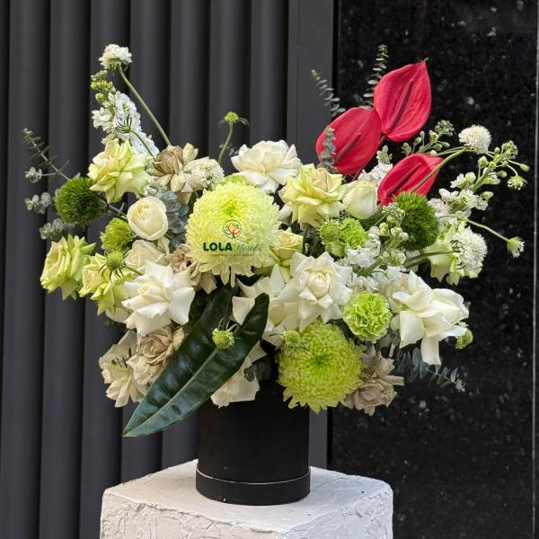 Mixed floral arrangement with white, green, and red blooms in a black vase