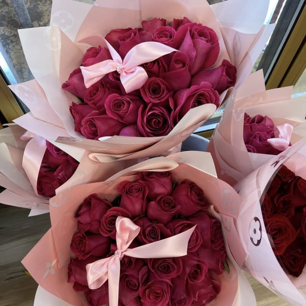 Bouquets of deep pink roses wrapped in pale pink paper with satin bows