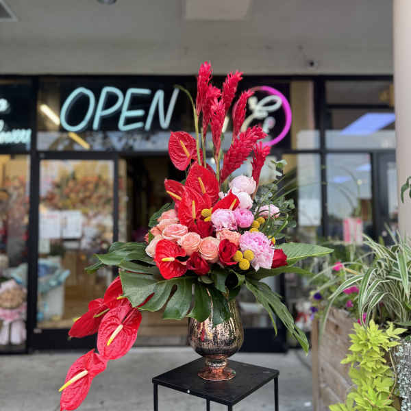 Tall arrangement of red anthuriums and pink flowers in a metallic vase