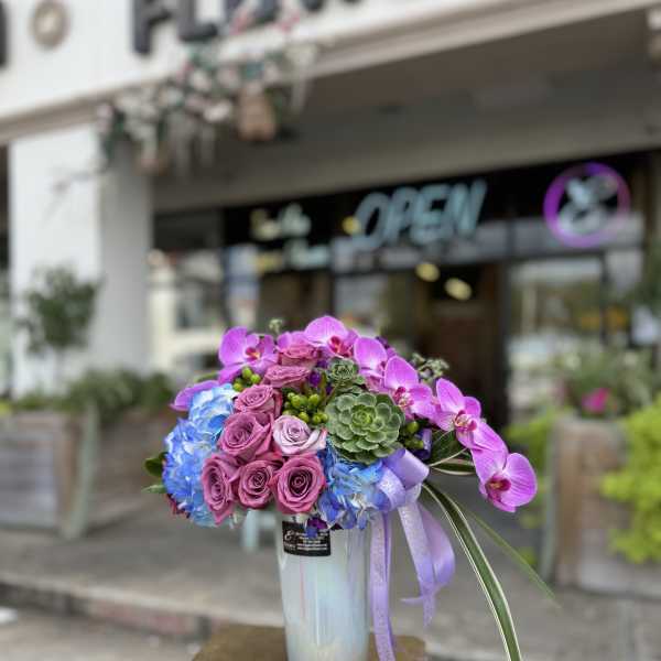 Bouquet of purple roses, blue hydrangeas, and orchids in a glass vase