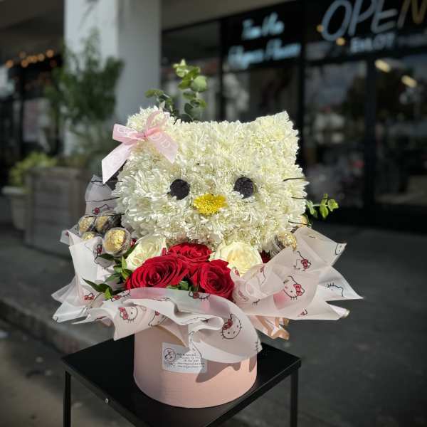 Cat-shaped flower arrangement with white blooms and red roses in a pink box