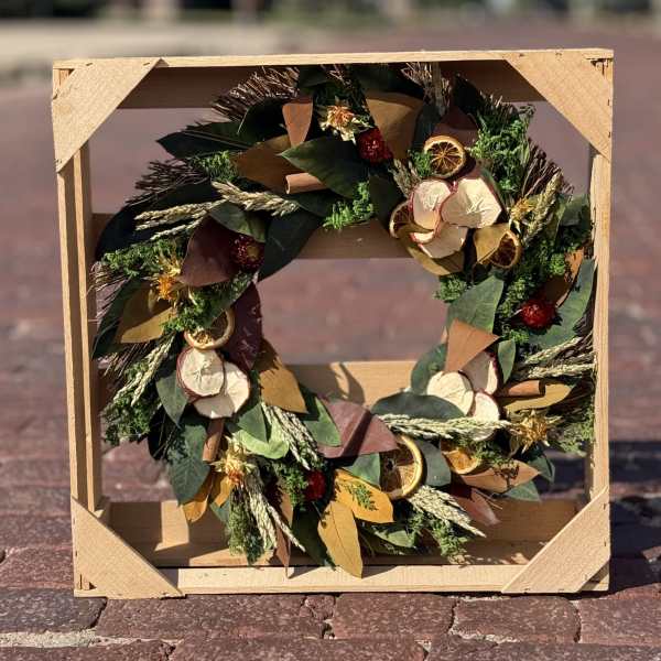 A decorative wreath with dried citrus slices and foliage in a wooden crate