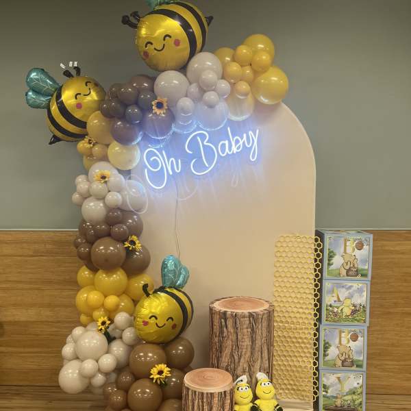 Bee-themed baby shower display with balloons, neon sign, and plush bees