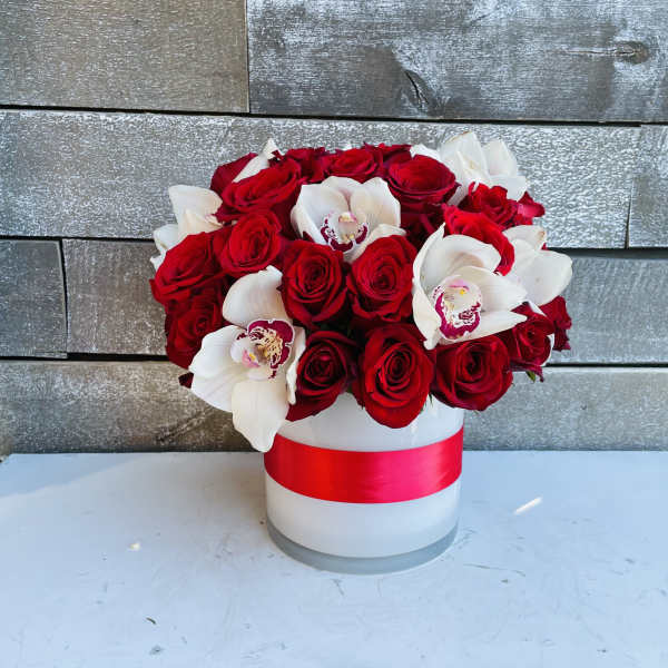 Red roses and white orchids in a white hat box with a red ribbon