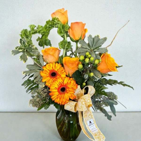 Orange roses and gerbera daisies in a glass vase with a ribbon