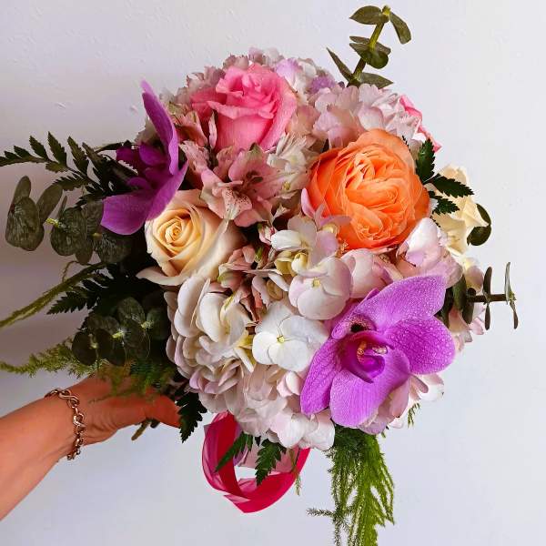Handheld bouquet of pink, orange, and purple flowers with a ribbon