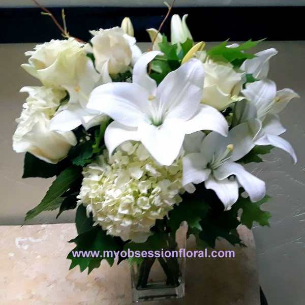 White lilies and roses arranged in a clear glass vase