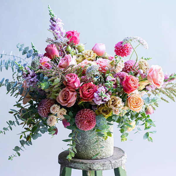 Large mixed bouquet of pink and peach flowers in a textured vase