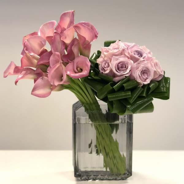 Modern arrangement of pink calla lilies and pale lavender roses in a rectangular glass vase