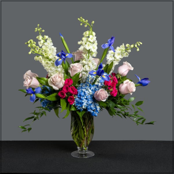 Mixed bouquet of roses, hydrangeas, and blue irises in a glass vase