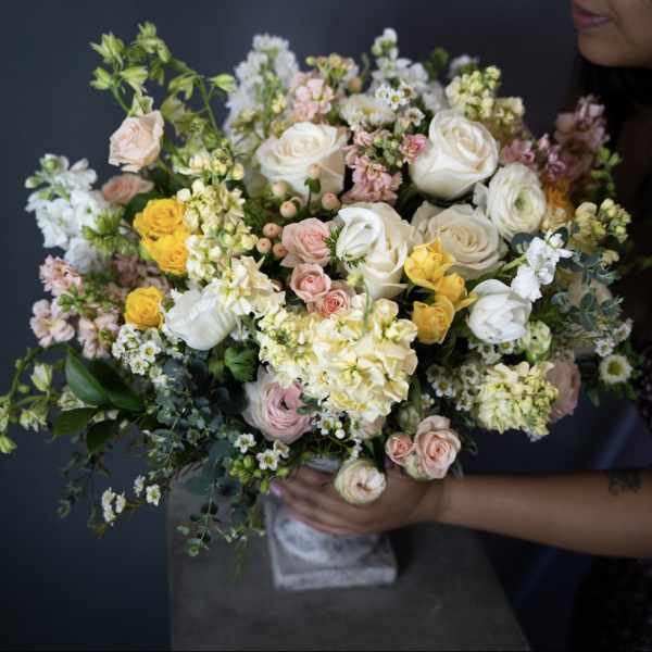 Large bouquet of white, pink, and yellow flowers held by a person