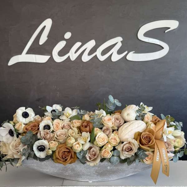 Long low floral arrangement with cream and peach blooms in a silver container