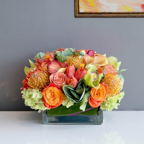 Colorful bouquet of roses, calla lilies, and tropical blooms in a glass vase