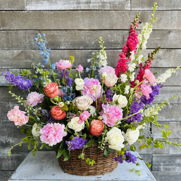 Mixed bouquet in a wicker basket with pink, white, purple, and blue flowers