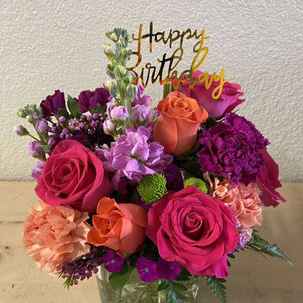 Bright mixed bouquet in a glass vase with a birthday topper