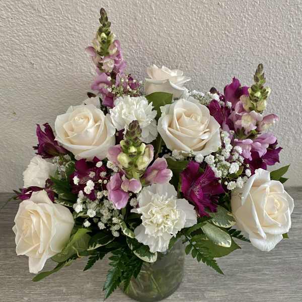 Bouquet of white roses, pink snapdragons, and white carnations in a glass vase